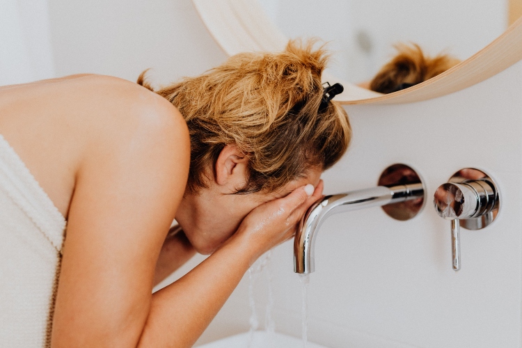 Persona lavándose el rostro con agua fría en un baño de oficina para recuperar energía y concentración durante la tarde.